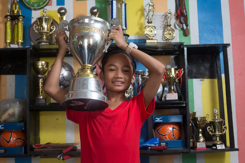 A young boy holding up his football trophy in a slum of Philippines