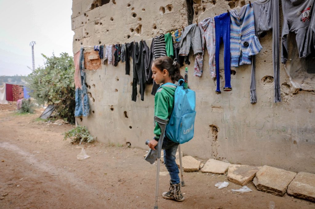 Disabled girl with one leg using crutches to move around in the street, wearing a unicef backpack