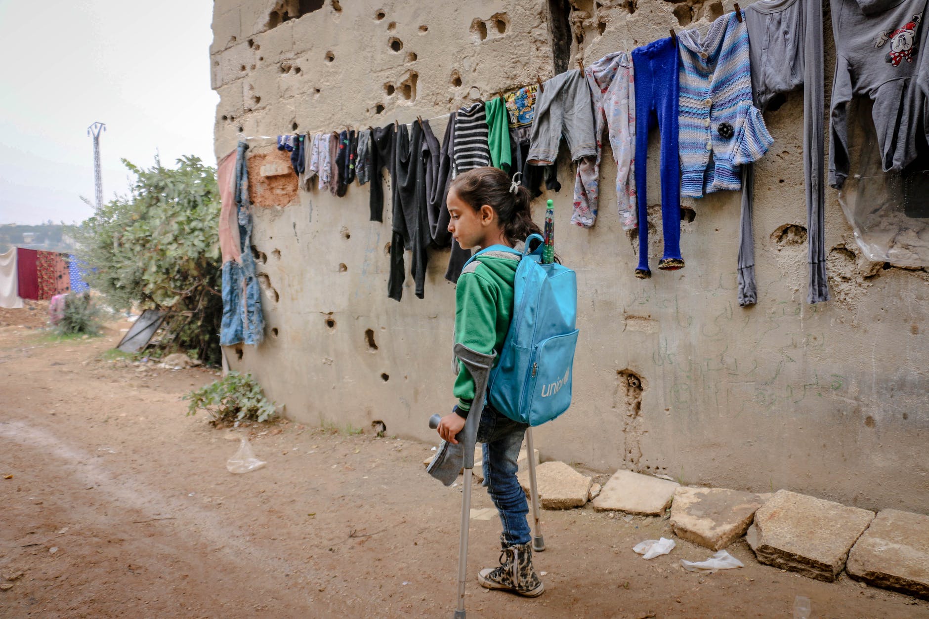 Disabled girl with one leg using crutches to move around in the street, wearing a unicef backpack
