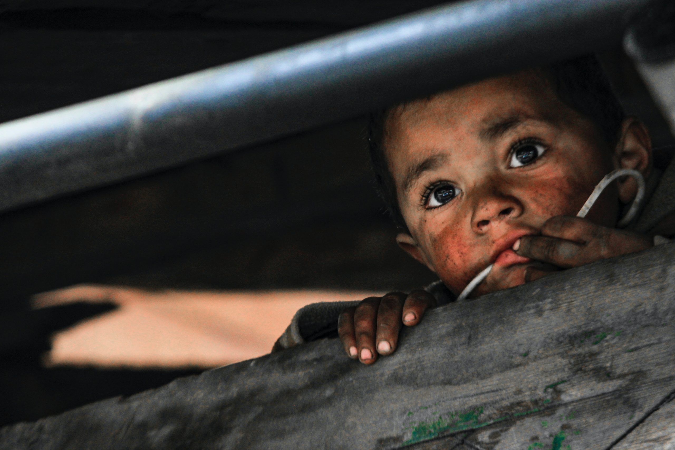 young boy looking scared, hiding between some wooden planks.