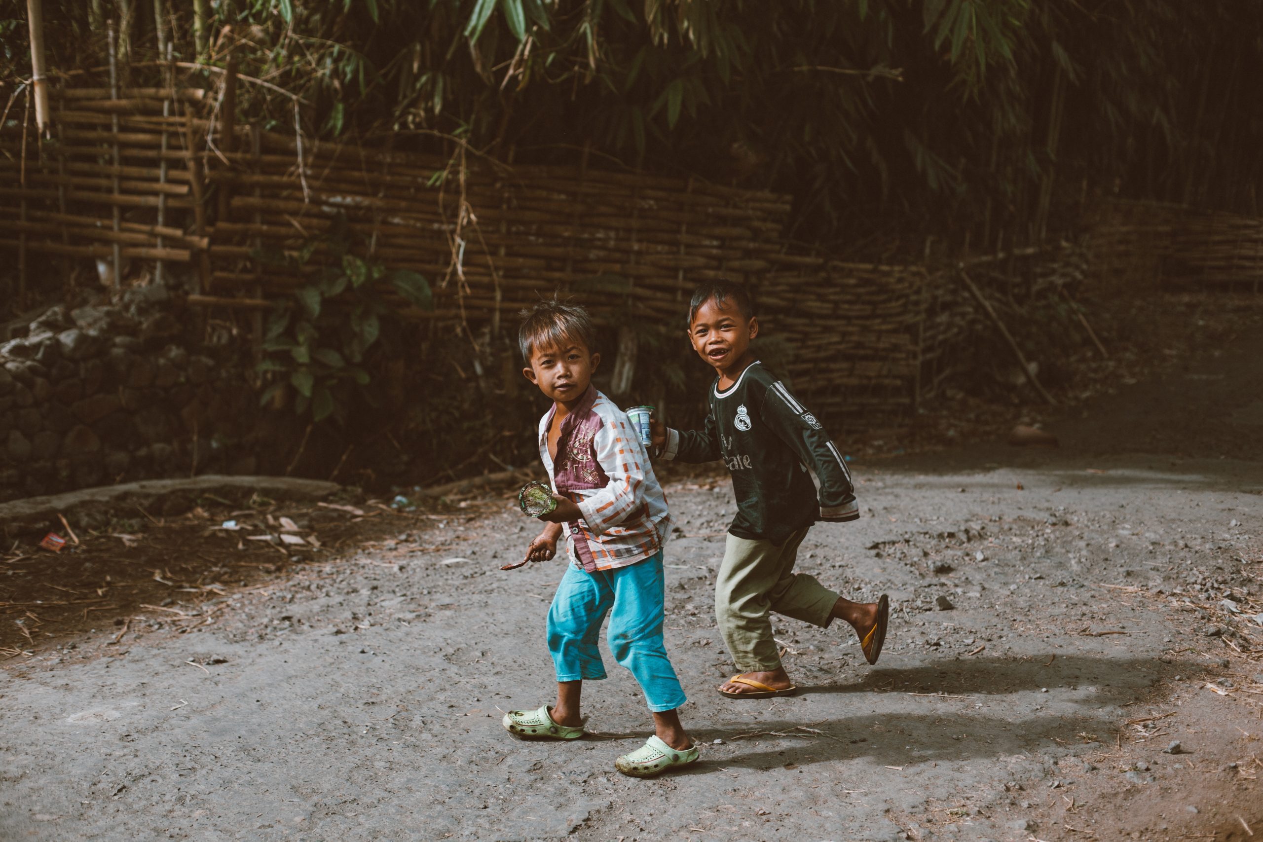 two young boys running in muddy clothes, smiling at the camera.