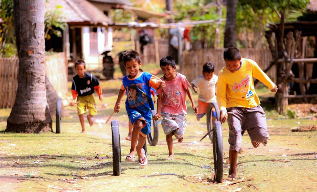 5 boys running and laughing, playing with tire and stick